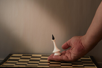 A person's hand lowers a chess king onto the chessboard and the light falls not on the figure. The...