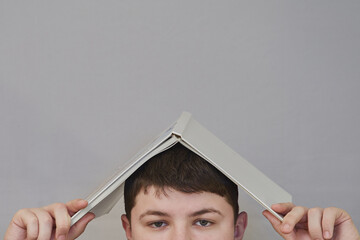 A child's hands holding a book over their head like a roof, space for caption. Books and children,...