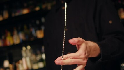 Bartender rotating long spoon behind the bar desk close-up. Night modern bar with many varius of drinks, cocktails 