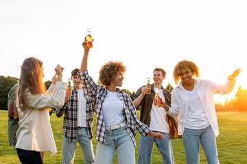 group of multiracial friends at party with bottles of beer dancing and having fun outdoors, group of people singing