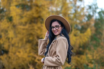 Portrait of a beautiful brunette woman in a beige coat and hat in the autumn park.