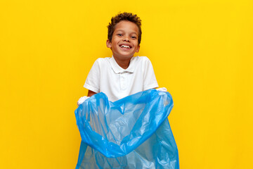 african american boy volunteer holding garbage bag and smiling on yellow isolated background