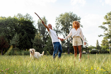 african american happy couple walk and run together with dog in park in summer
