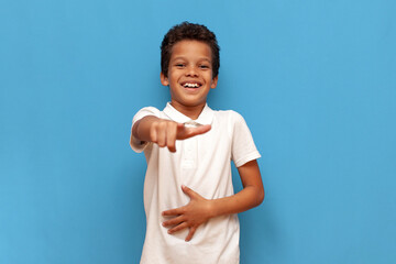 african american teenage boy in white polo taunts and jokes and points with hand forward on blue...