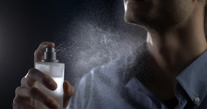 Anonymous man spraying luxury fragrance in extreme slow motion with scent particles to wet skin after dressing . concept of men's perfume and aftershave sensual men. Man perfumed after shave