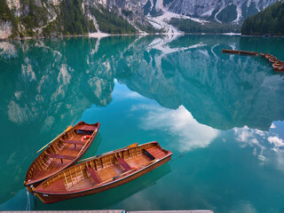 Two wooden boats on a blue-green water surface of Lago di Braies, mirroring Dolomite peaks. Ideal for poster projects.
