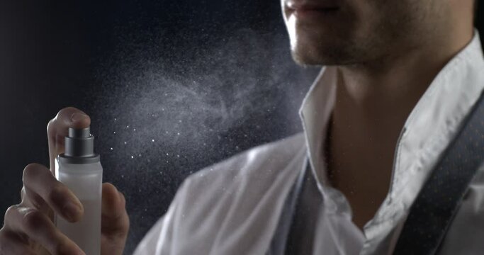 Anonymous man spraying luxury fragrance in extreme slow motion with scent particles to wet skin after dressing . concept of men's perfume and aftershave sensual men. Man perfumed after shave