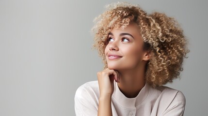 Appealing youthful african-american female student with light hair holding hand on chin and looking enchanted at upper cleared out corner as considering, posturing keen satisfied with - obrazy, fototapety, plakaty