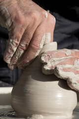 The hands of a master potter working his product on a potter's wheel.