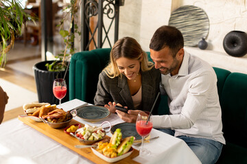 Young couple having lunch and drinking fresh squeezed juice while looking at the mobile phone in...