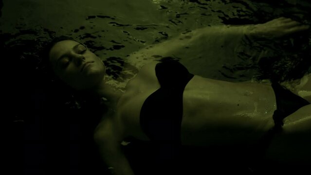 Beautiful fit sexy girl in bikini lying in dark water with colorful side light..