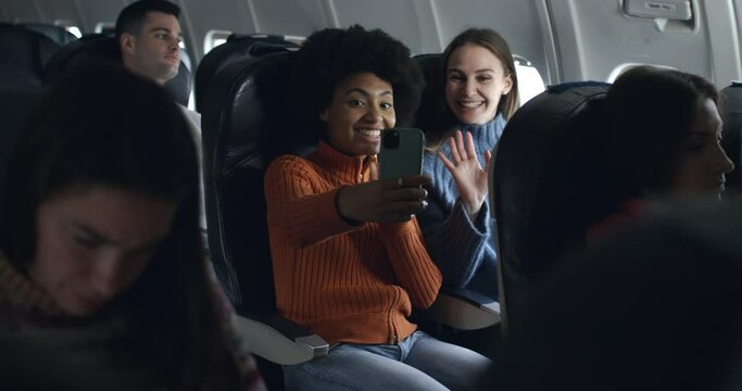Young woman with afro hair and friends in airplane have a nice moment together and having fun taking pictures and video call and laughing in friendship during flight to holiday vacation destination.