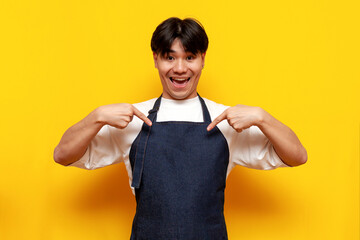 asian young male waiter in apron pointing to himself on yellow isolated background, korean guy barista businessma
