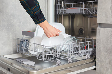 A woman's hands load and and takes out plates, cups and other dishes into an open dishwasher in a...