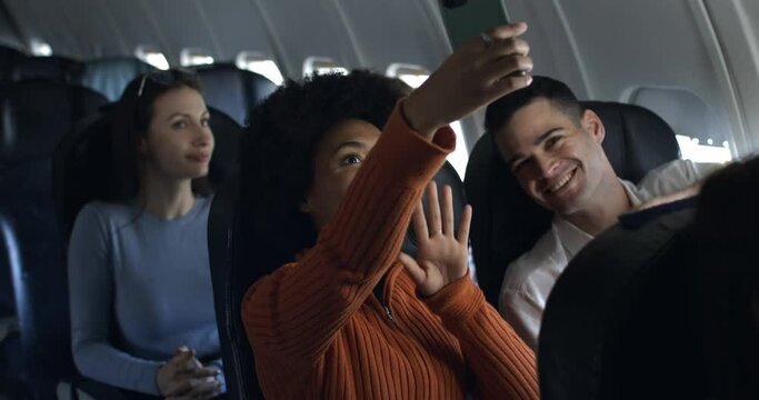Young woman with afro hair and friends in airplane have a nice moment together and having fun taking pictures and video call and laughing in friendship during the flight from the distant airport.
