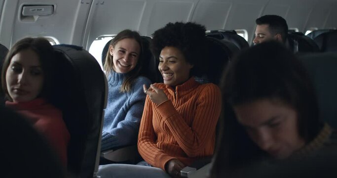 afro girl and blonde friend in airplane have a nice moment together and having fun talking and laughing in friendship during the flight from the distant airport.