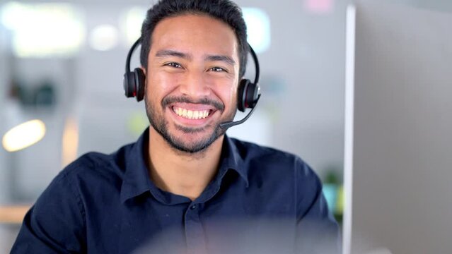 Laughing call centre agent helping customers while wearing a headset and typing on a computer to answer questions. Portrait of a friendly and cheerful male customer service operator in his office