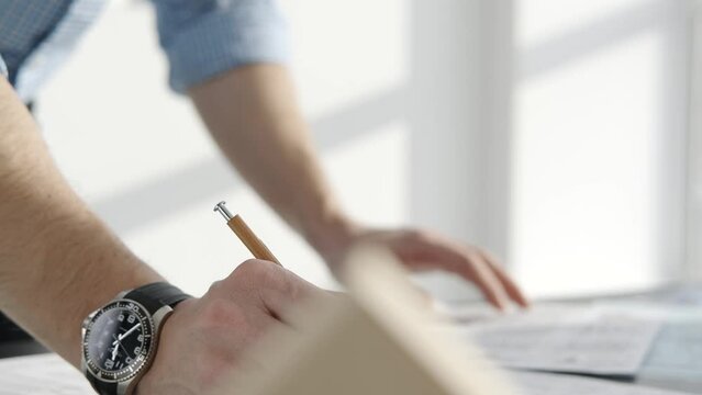 Male hand with a pencil: close-up. He writes on paper, only hands in the frame. No face.
