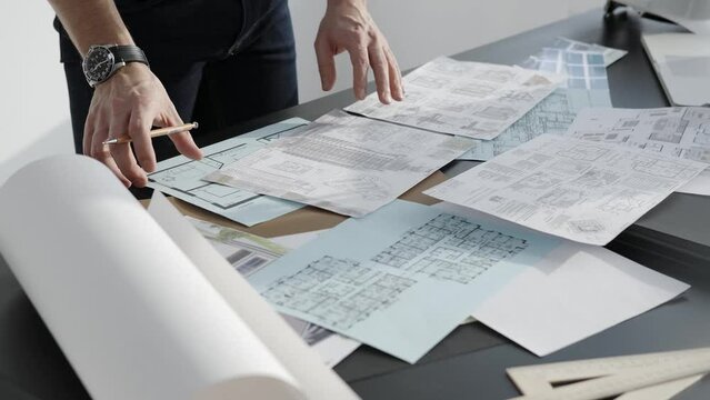 A man makes a project of the future home, a professional designer. Drawings and helmet on the table. Close up.