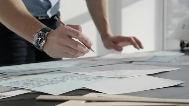 The architect works with drawings on the table. Close-up, only hands in the frame.