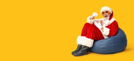 Santa Claus eating popcorn and watching Christmas movie against yellow background with space for text