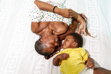 Affectionate African mom and son laughing together on a cozy blanket, enjoying family time.