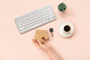 Female hand with wooden house figure, key, keyboard and coffee on pink background. Concept of...