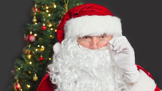 Close-up portrait of Santa Claus adjusting his glasses and winking with one eye