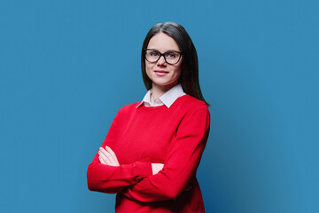 Fototapeta premium Young smiling woman with crossed arms looking at camera on blue background
