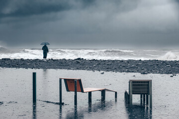 man on the shore near the sea, ocean in a raincoat and with an umbrella during a storm, hurricane,...