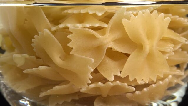 Authentic italian dry pasta farfalle rotating in glass bowl. Raw dried organic golden macaroni, traditional Italy food