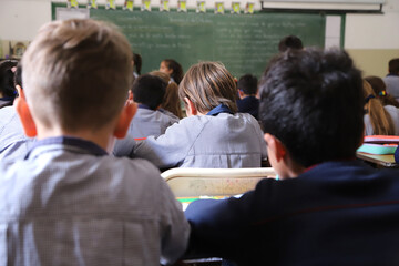 Primary school with children studying.Students in class copying text from the blackboard. Classroom with green blackboard in the background and students. Background with copy space.