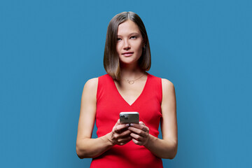 Young woman with smartphone in hands on blue studio background