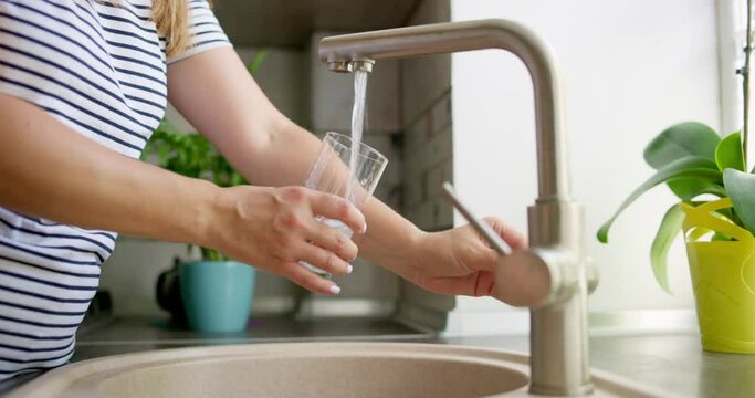 Woman pouring clean filtered water from the tap in glass at kitchen