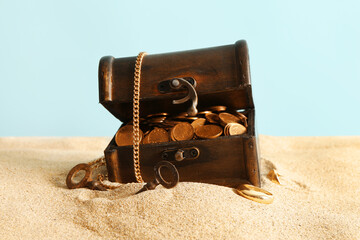 Old chest with treasures and keys on sand against blue background