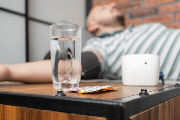 Defocused background with man who has hypertension and headache, lying on sofa at home, measures...