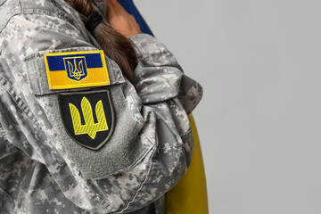 Female soldier in uniform with Ukrainian flag patch on sleeve against grey background, closeup