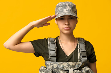Confident young female soldier in uniform saluting on yellow background