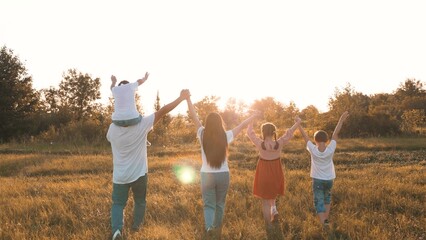 Strong friendly family with children walks raising hands across meadow at sunset