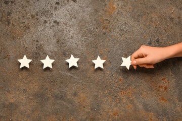 Female hand with five stars rating on rusted metal background. Customer experience concept