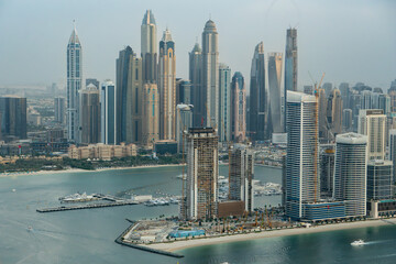 Aerial view of Dubai Marina, UAE, with many tall skyscrapers. Hazy day, boats in the marina. At sunset