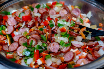 Close-up of the texture of the ingredients. Vegetables with vivid colors. preparation of a dish with vegetables, ingredients for Stew with peppers and sausage, hand stirs the food