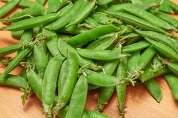 green ripe plucked pea pods on a wooden kitchen cutting board close-up