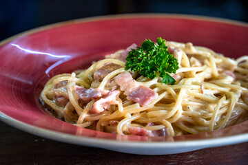 a freshly prepared spaghetti carbonara served in a red bowl close up