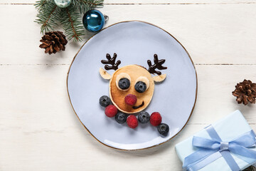 Plate with pancake in shape of reindeer on white wooden table. Christmas celebration