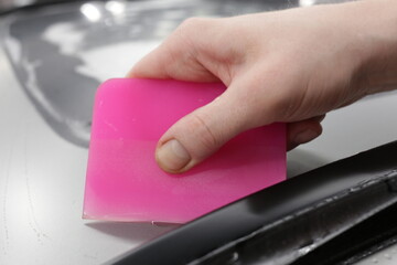 Wrapper holds squeegee and heat gun, wrapping car. A car wrapping specialist applies a polyurethane...