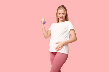 Beautiful young pregnant woman with dumbbell on pink background