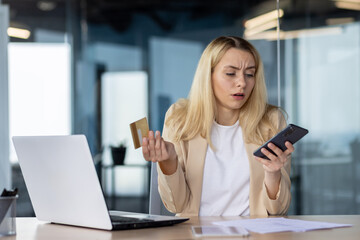 Frustrated sad upset woman working inside office, cheated business woman refused online money transfer, female worker displeased holding bank credit card and phone - obrazy, fototapety, plakaty