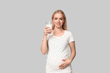 Beautiful young pregnant woman with glass of milk on grey background