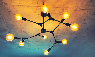 Light bulbs with warm lighting in stylish chandelier with exposed wiring on gray concrete ceiling,...